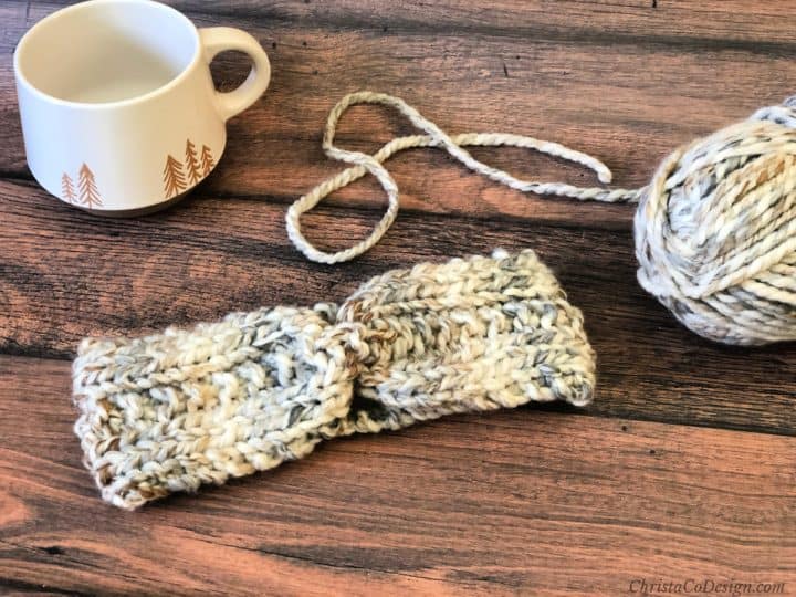 Chunky knit earwarmer on wood table with coffee cup and yarn.