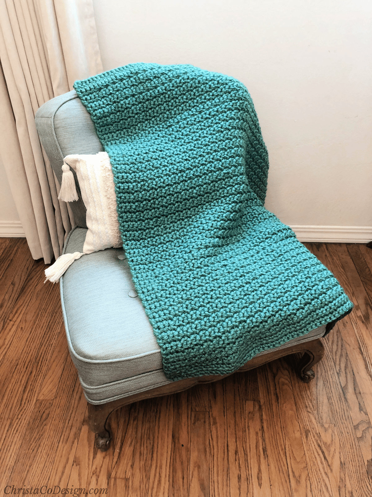 Chunky green crochet blanket draped on vintage blue chair in room with wood floor.