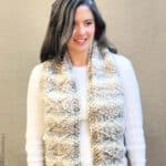 Woman in white sweater with knit scarf draped over front.