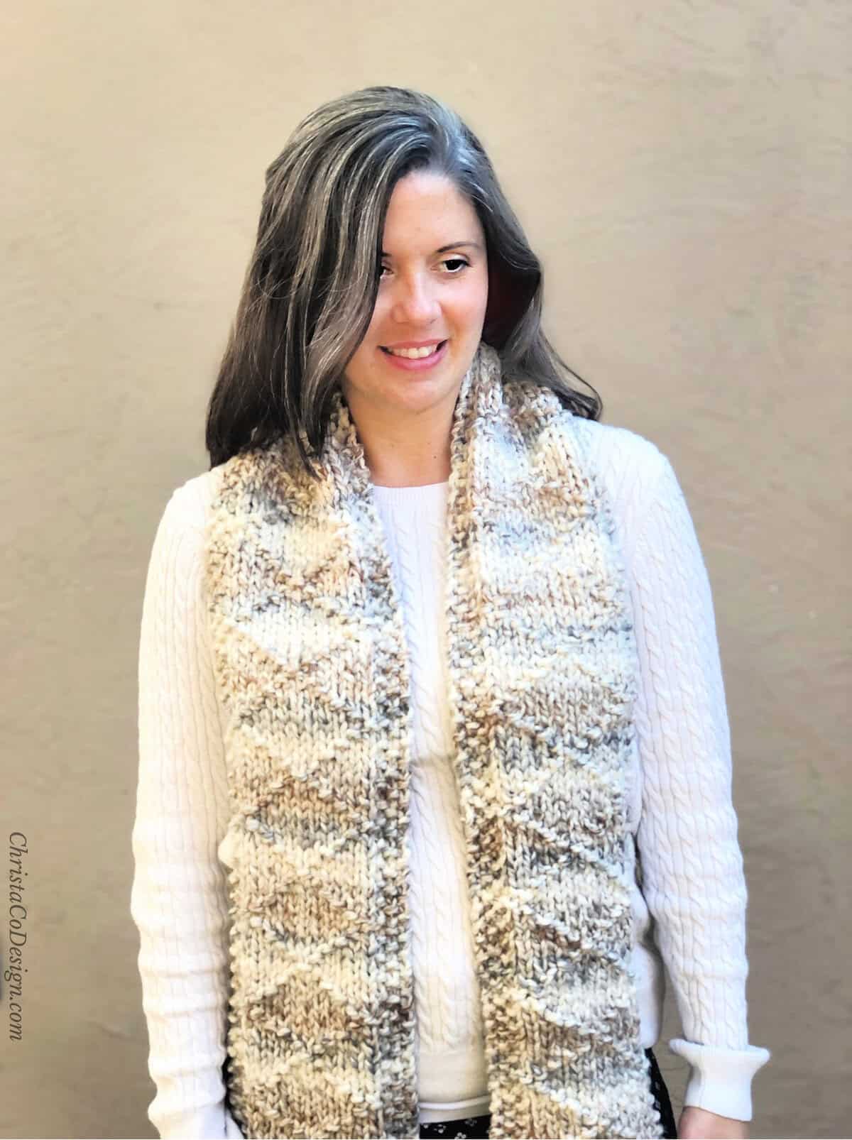 Woman in white sweater with knit scarf draped over front.