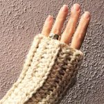 Woman's hand wrapped in cozy chunky fingerless glove in front of lavender wall.