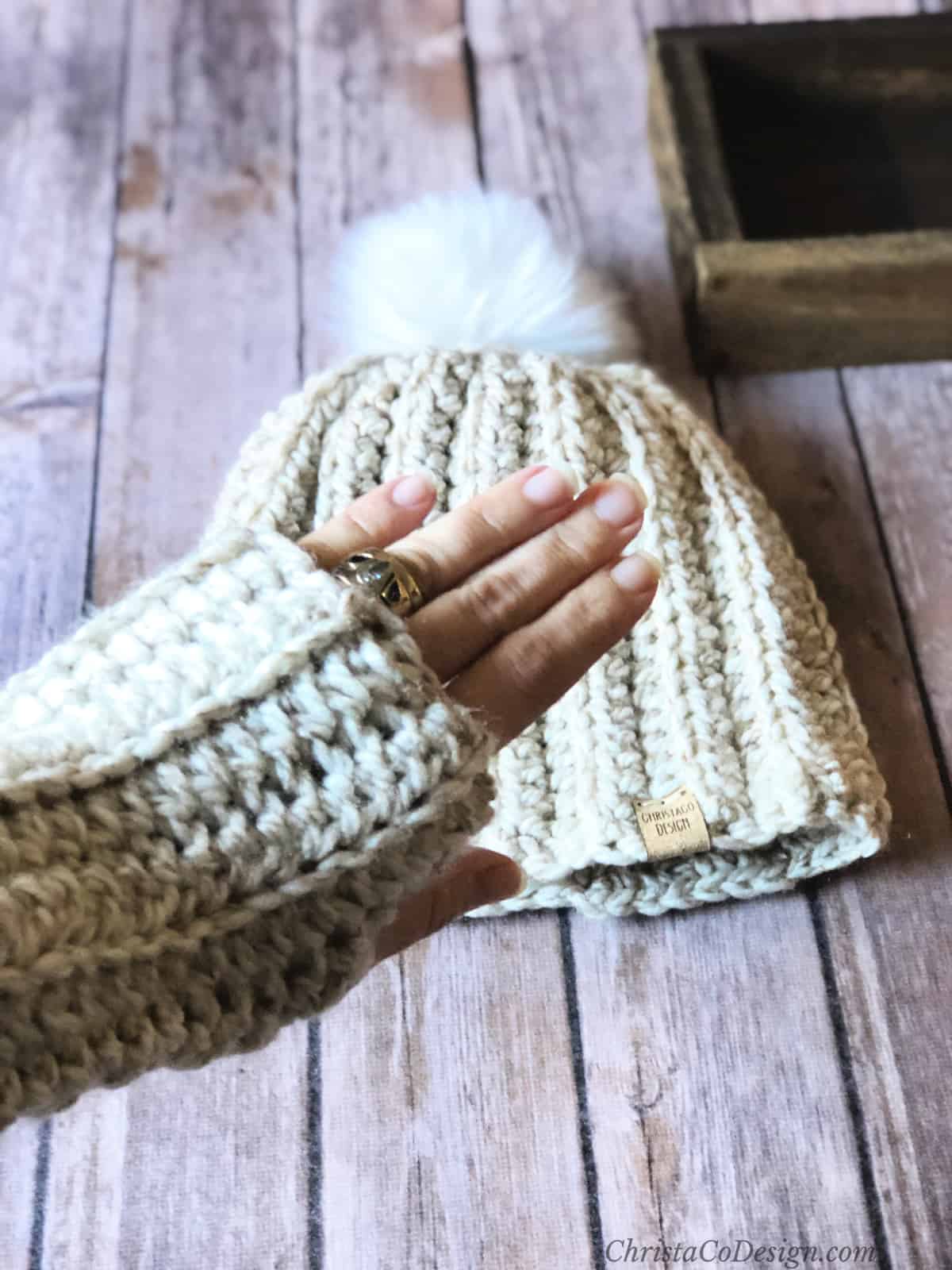 Woman's hand in chunky ribbed crochet fingerless glove over matching hat.