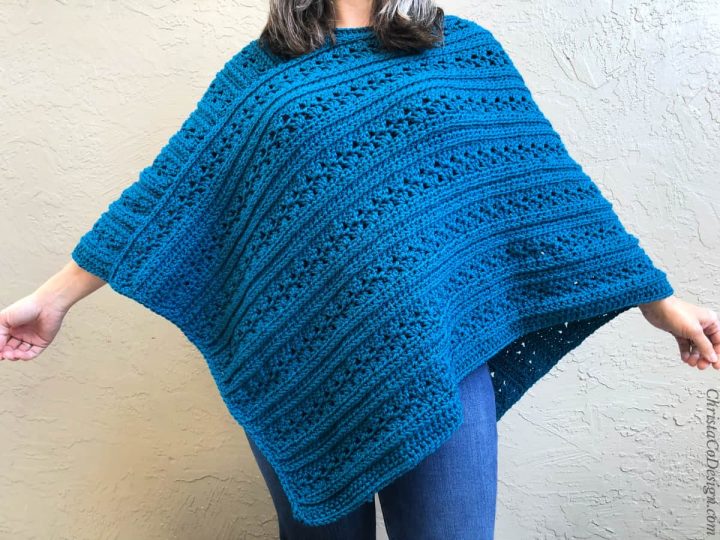 Woman with arms spread showing texture on blue crochet poncho.