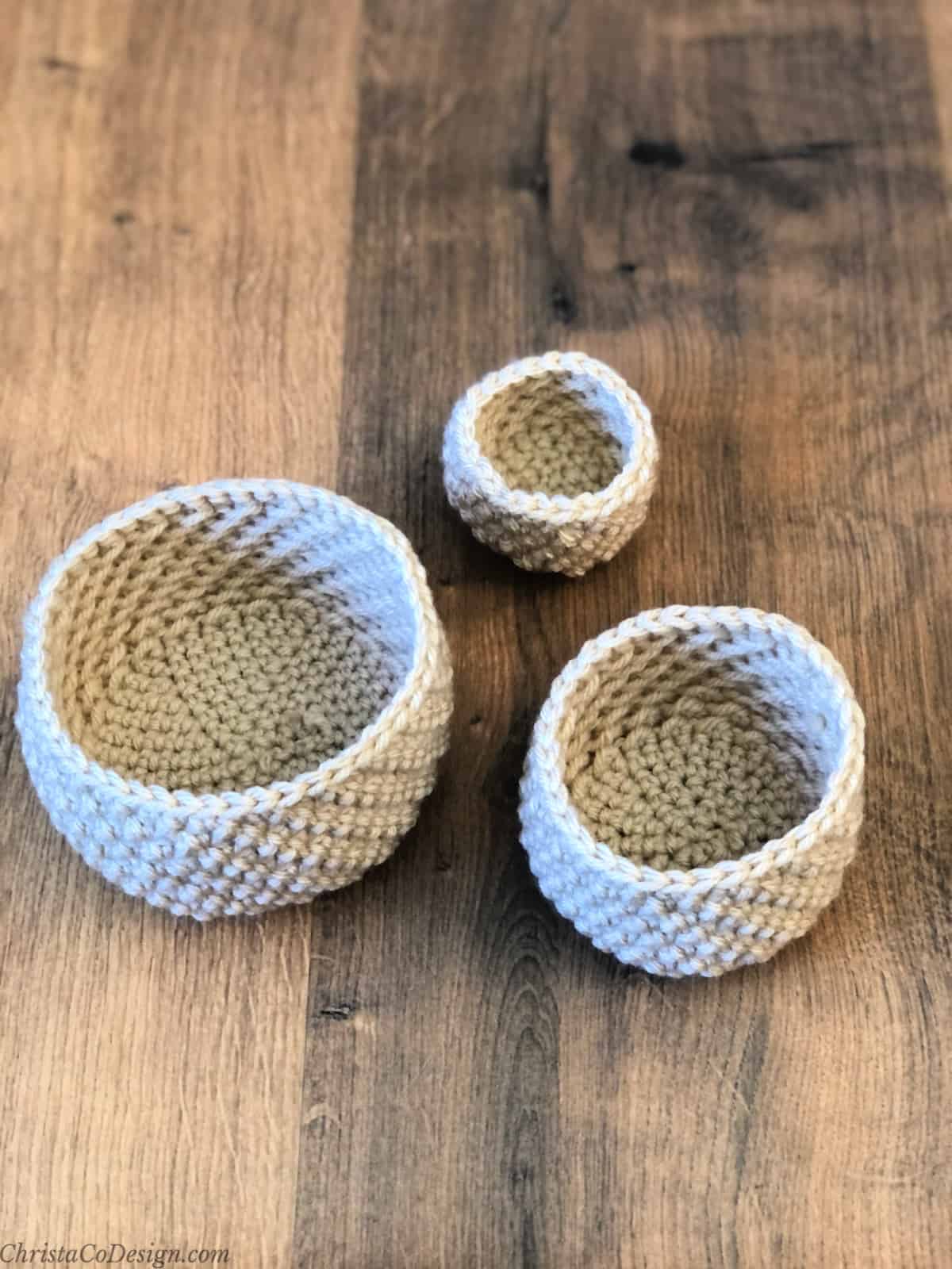 Three small crochet baskets set in a triangle on wood table.