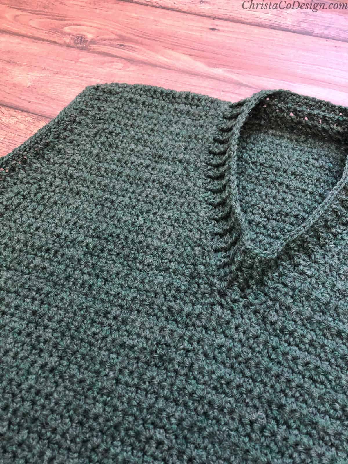 Neckline on men's crochet sweater vest in green on wood backdrop.