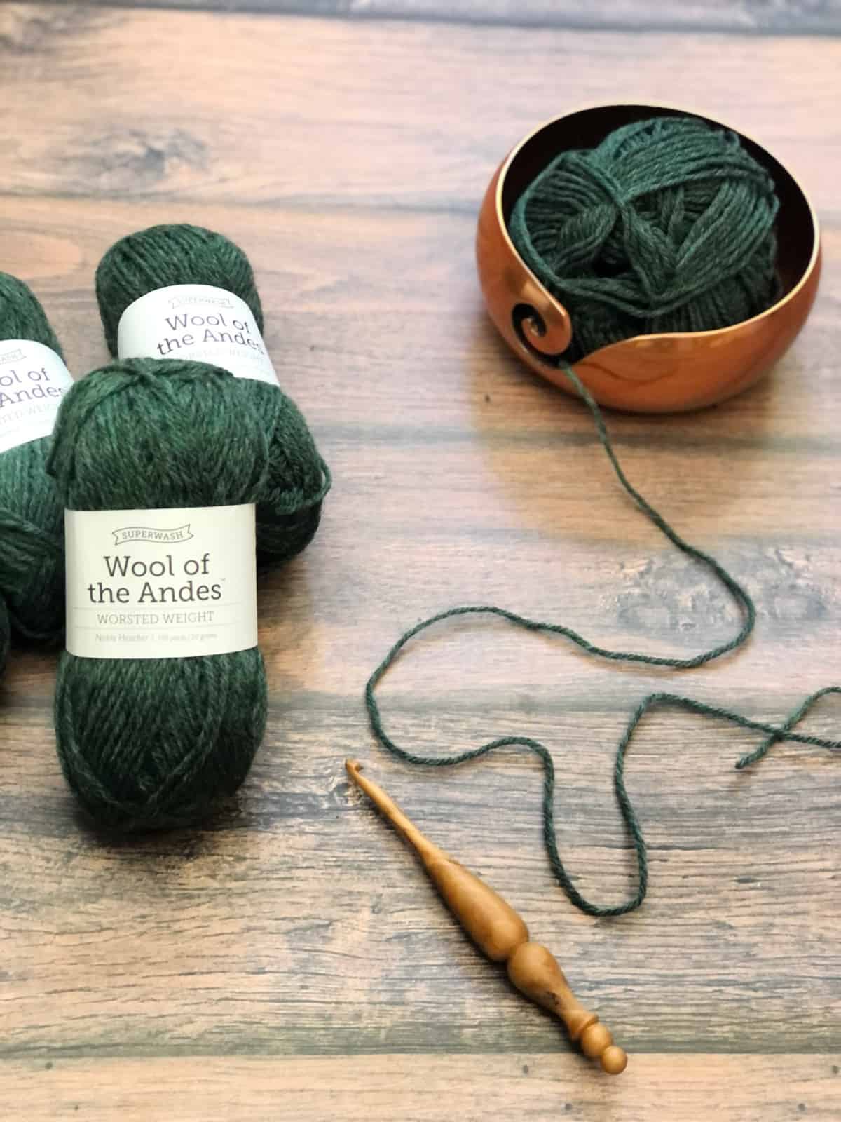 Green skeins of yarn and copper yarn bowl with ergonomic crochet hook.