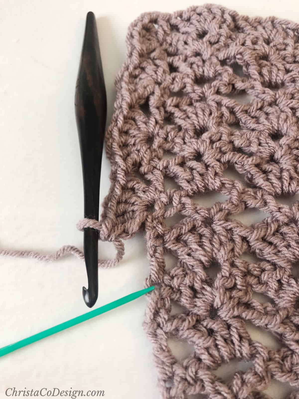 Green needle pointing where to start next shell stitch on shawl border.