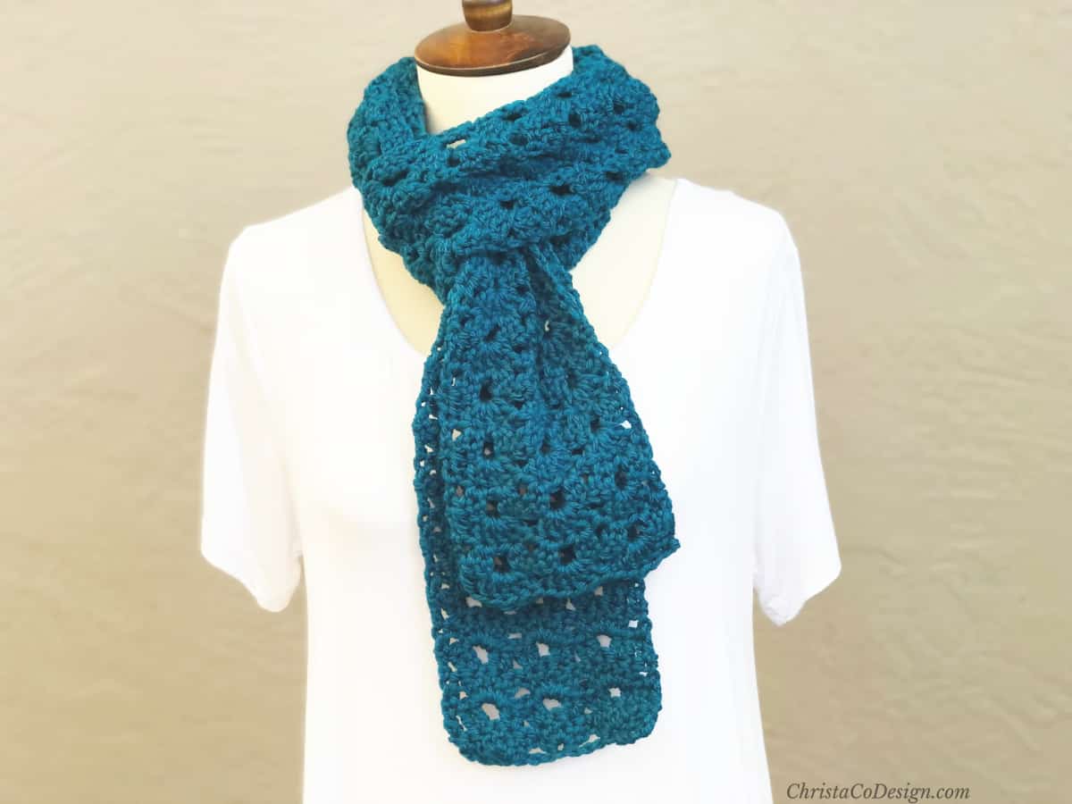 Mannequin in white wearing blue crochet scarf looped stylishly around neck.