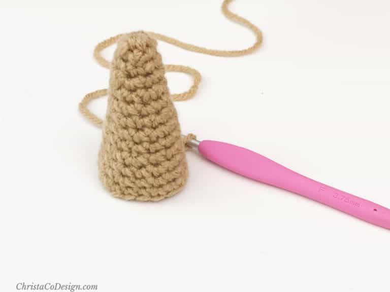 Brown crochet cone sits on white table next to pink crochet hook.