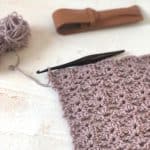 Progress of rectangle shawl in purple with crochet hook.