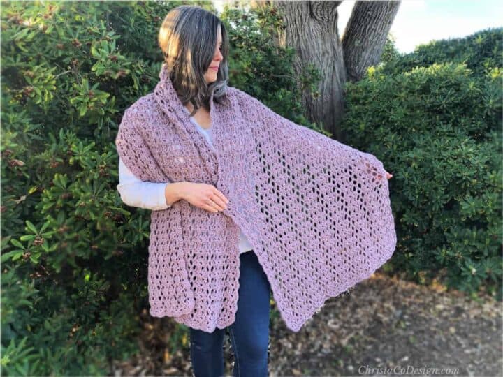 Woman holding purple crochet shawl outside to show lace.