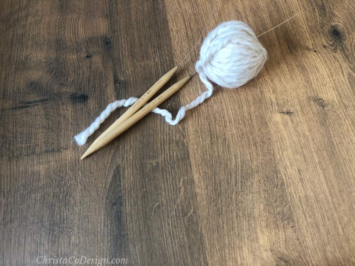 Wooden circular knitting needles with white ball of wool.