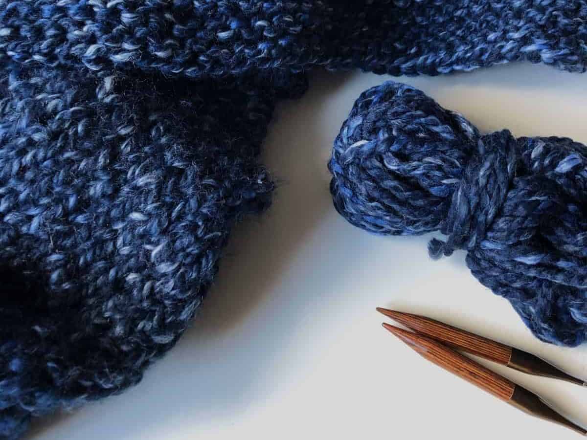 Picture of knitting needles and blue chunky yarn blanket.