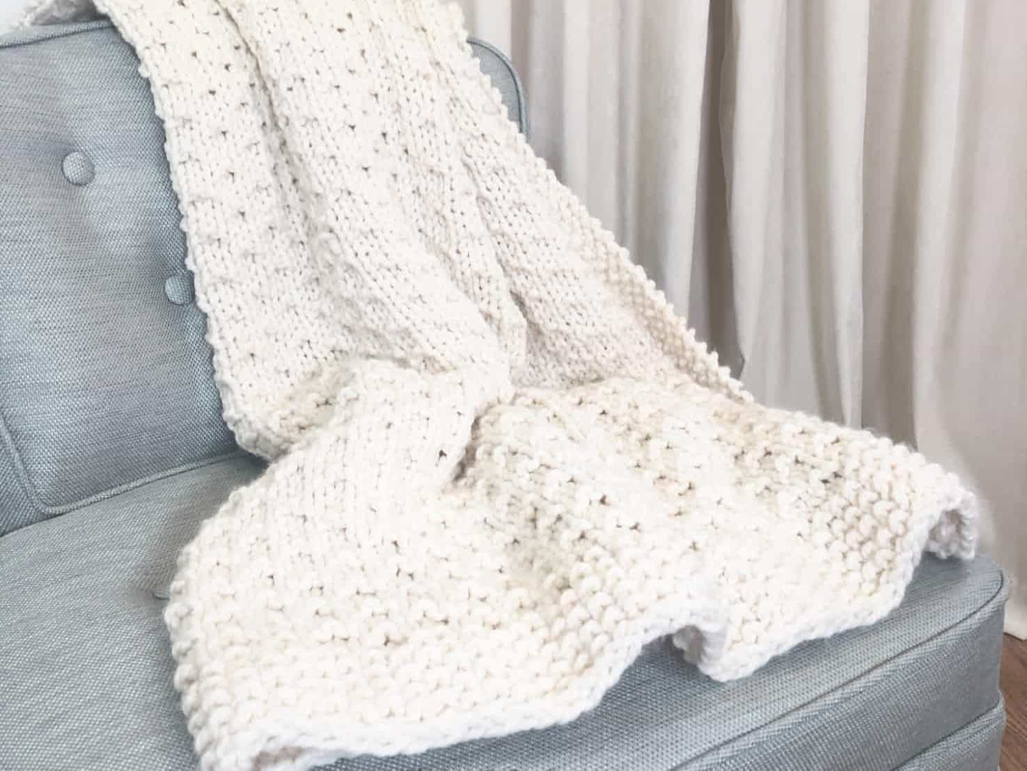 Bella vita easy knit blanket beginner knitting pattern in cream yarn on blue chair.