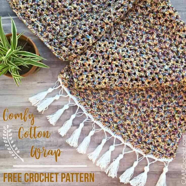 Crochet wrap with white fringe edge on table with potted plant.