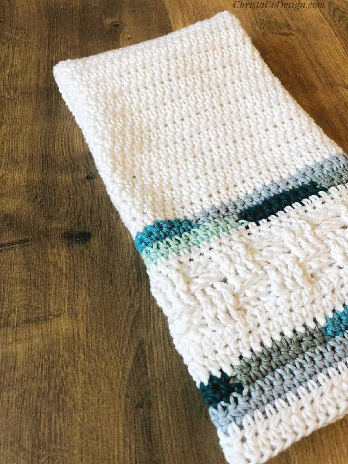 White crochet towel with blue stripes on wood table.
