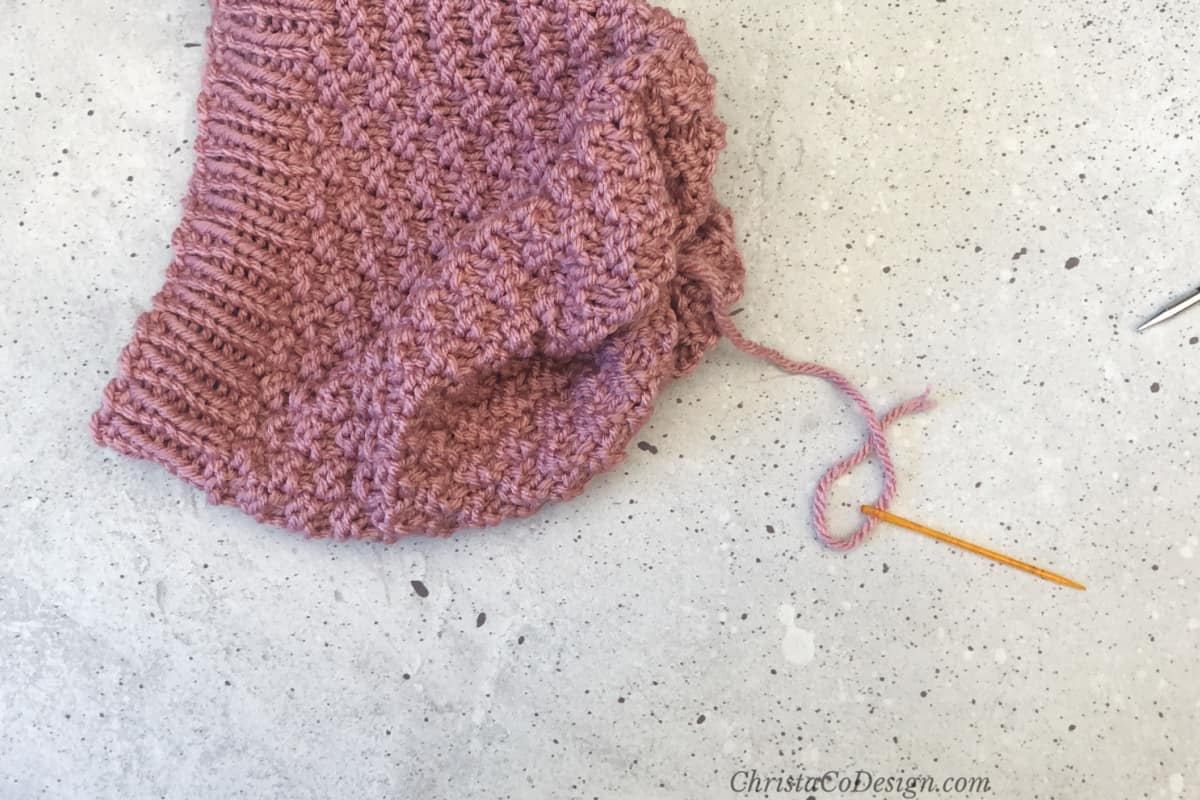 Pink knit hat cinched closed with yarn needle and tail.