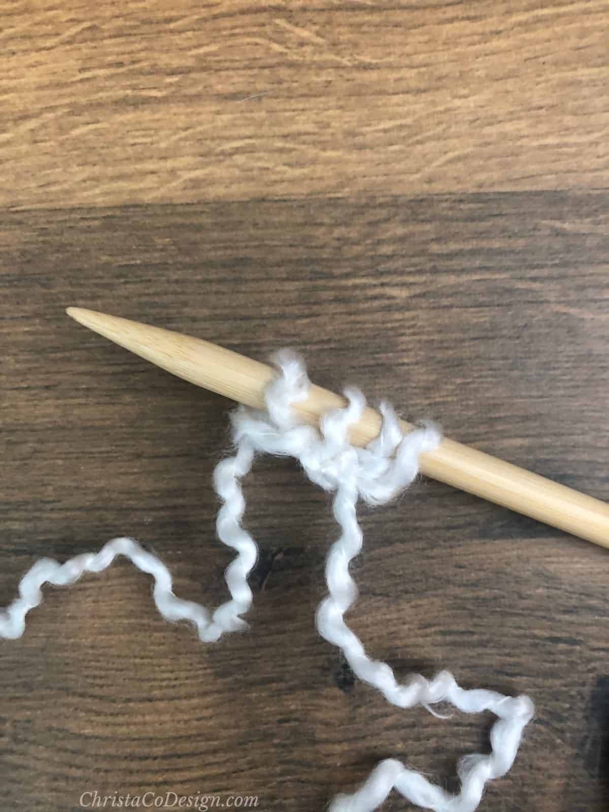 4 white stitches on knitting needle.