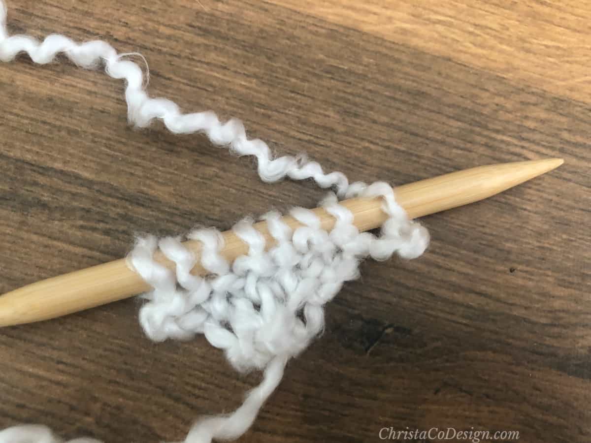 Chunky white yarn with kfb knitting increases on needle.