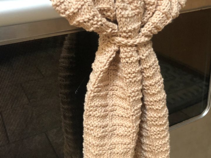 Beige textured knit towel hanging from stainless steel oven bar.