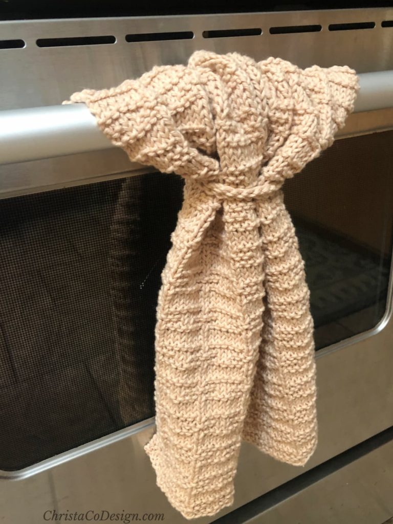 Beige textured knit towel hanging from stainless steel oven bar.