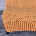 Orange crochet blanket draped over chair showing ribbing edge.