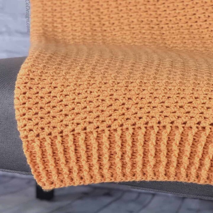 Orange crochet blanket draped over chair showing ribbing edge.