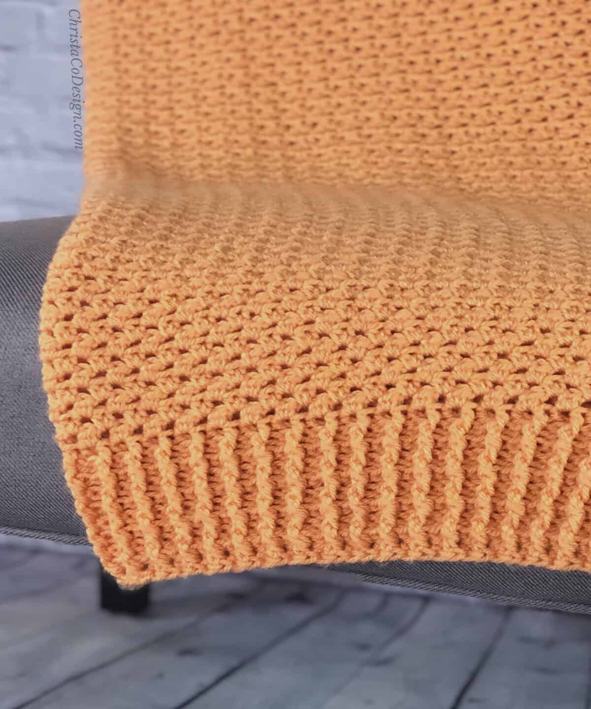 Orange crochet blanket draped over chair showing ribbing edge.