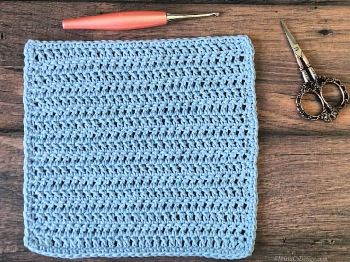 Blue crochet dishcloth with hook and scissors.