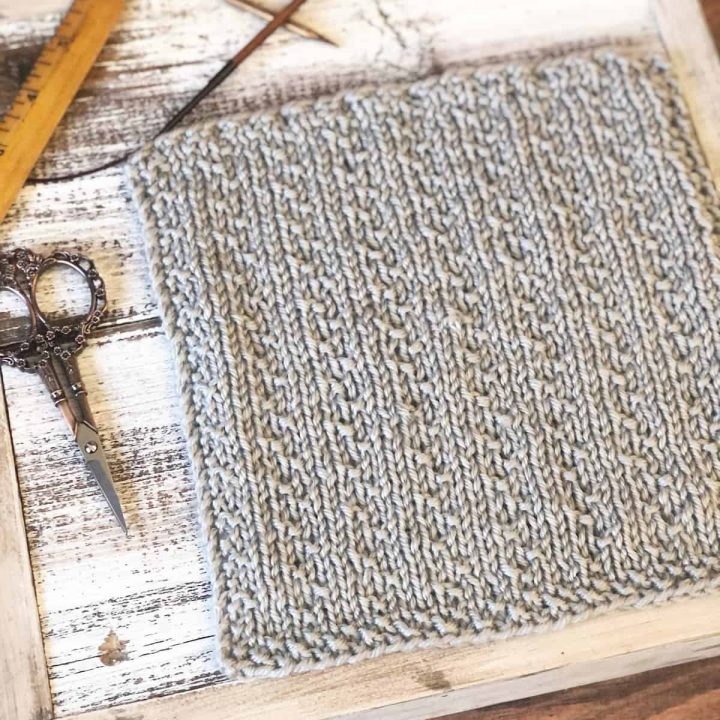 Grey knit square with textured columns on white wood square with knitting notions.