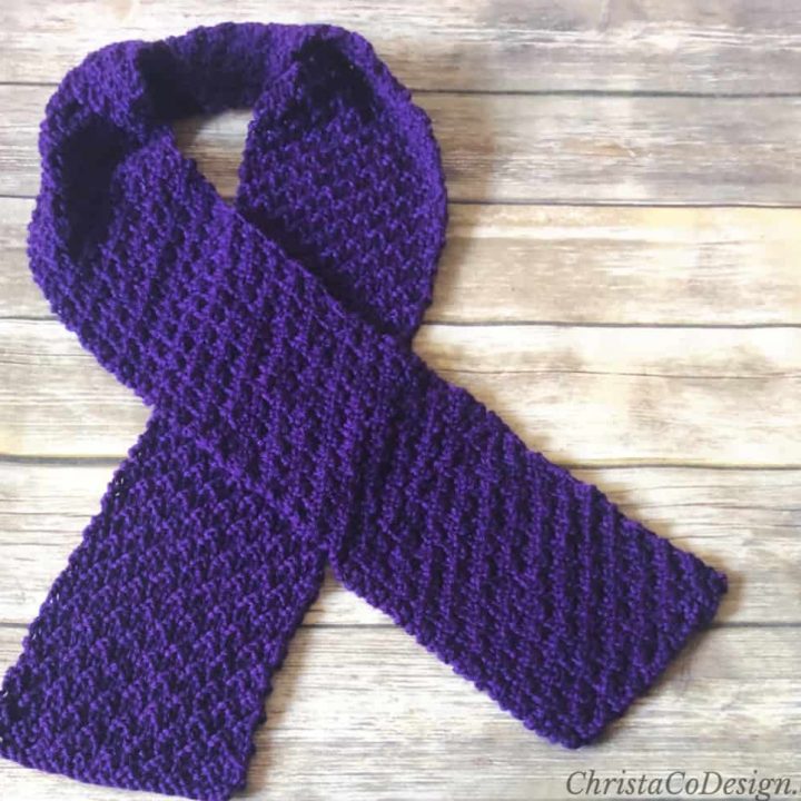 Purple knit scarf crossed flat on wood table.