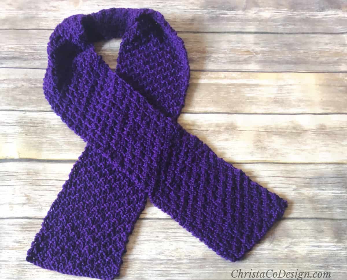 Purple knit scarf crossed flat on wood table.