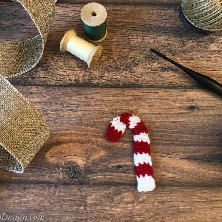 Crochet candy cane on wood table with spools and ribbon.