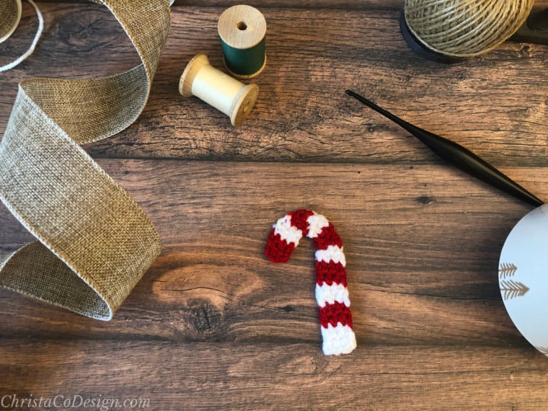 Crochet candy cane on wood table with spools and ribbon.