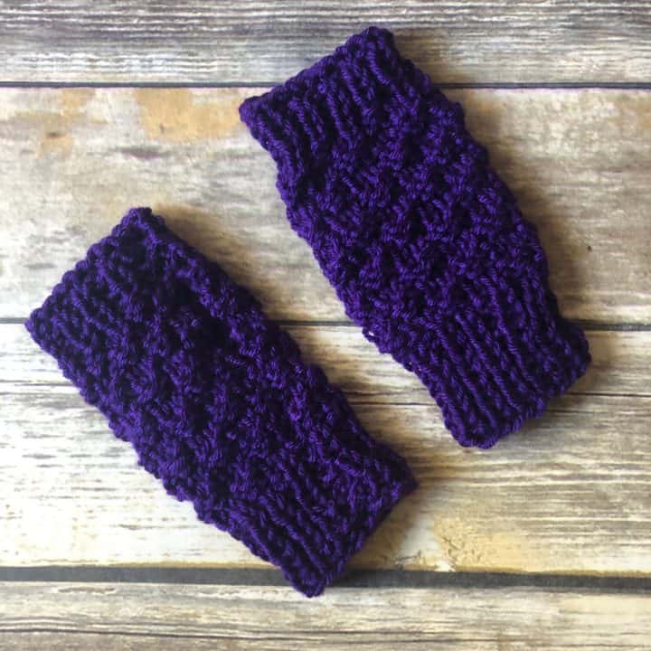 Two purple knit fingerless gloves on wood table.