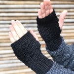 Black knit fingerless gloves on man's hands in front of tan bamboo wall.