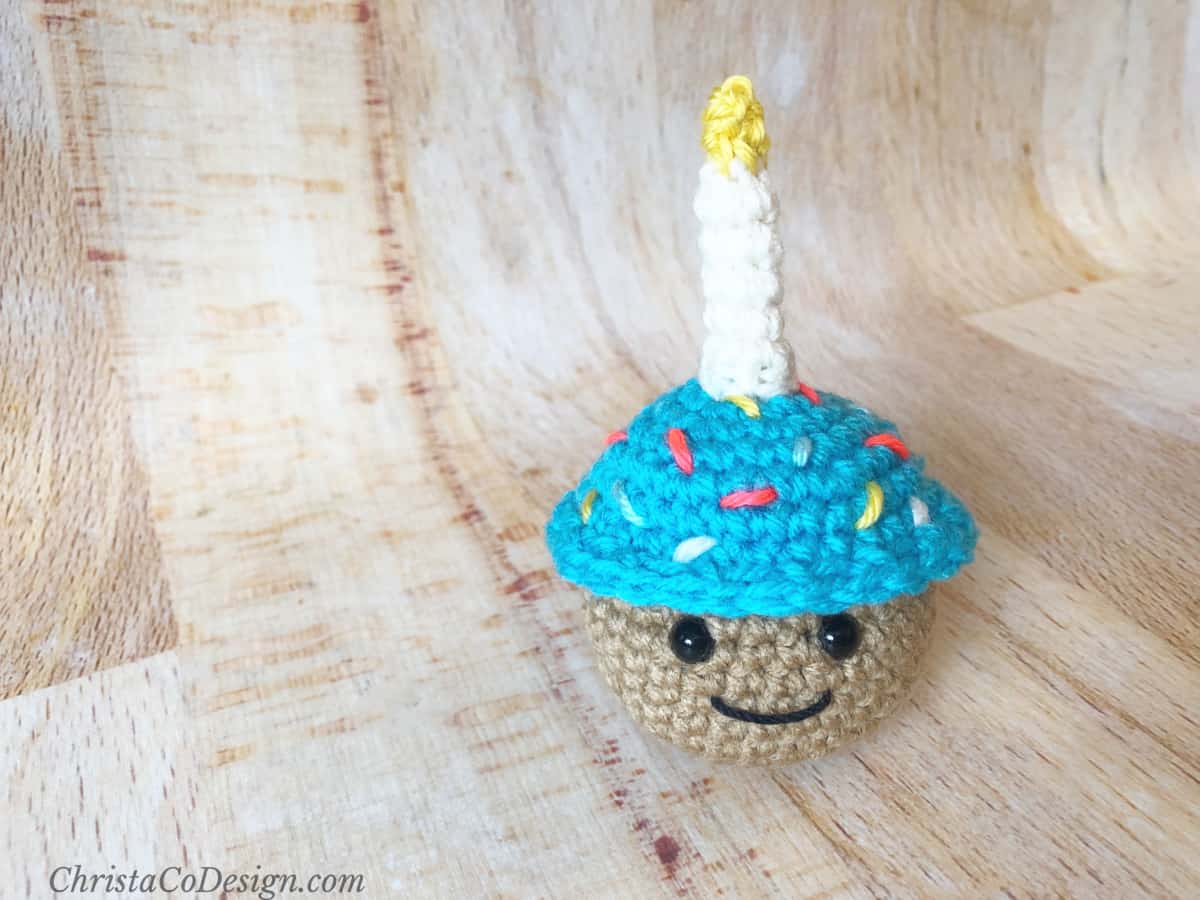 Crochet cupcake with blue frosting and white candle.