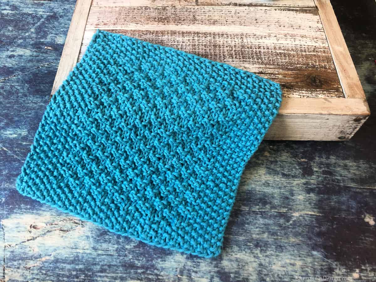 Blue knit dishcloth draped on wood box.