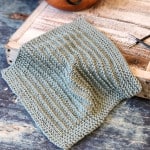 Sage green knit dishcloth on white wood board.