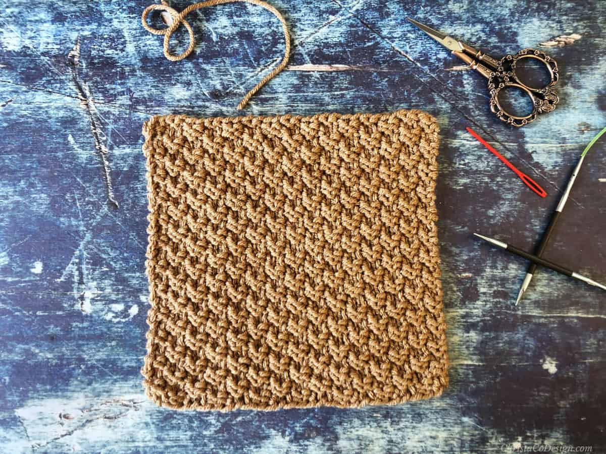 Brown knitted swatch of double moss stitch on blue background.