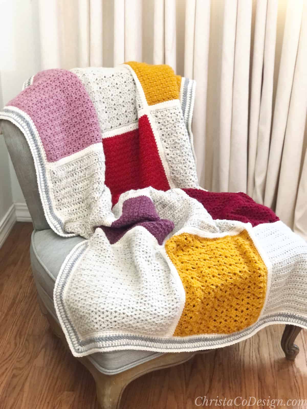 Patchwork crochet blanket in pink, red, gold and cream draped over chair.