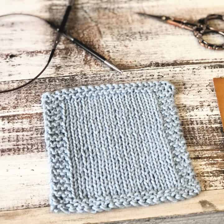 Pale blue knit coaster on white wood with notions.