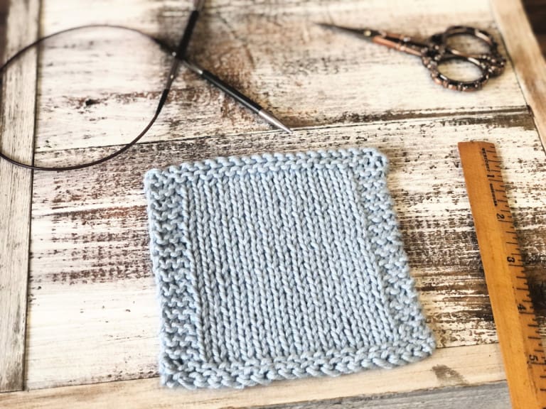 Pale blue knit coaster on white wood with notions.