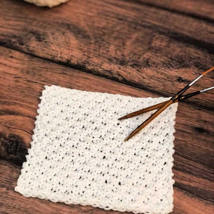 White dishcloth with knitting needles and yarn on table.