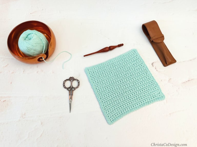 Mint colored yarn and dishcloth layer out with hook, scissors and case.