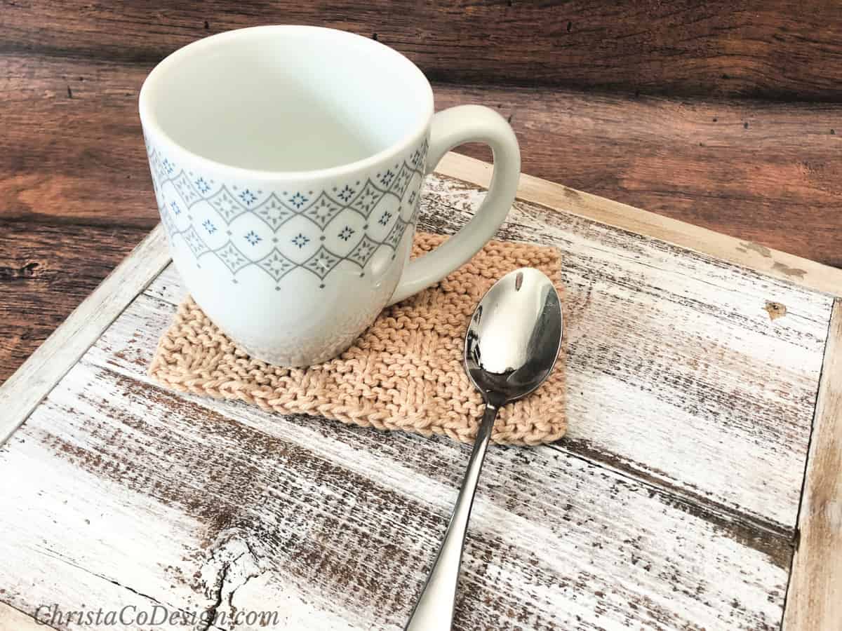 Coffee cup on beige mug rug with spoon.