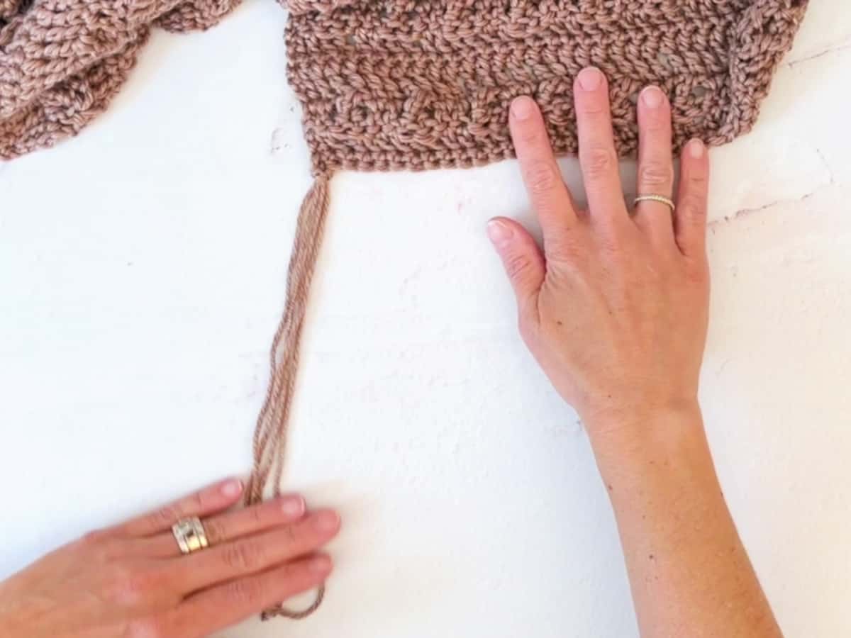 Hands holding scarf and lengths of yarn fringe.