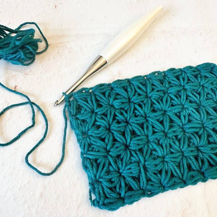 Teal swatch of jasmine crochet stitch on white hook.