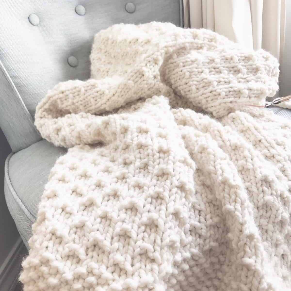 Chunky knit blanket in cream with dot texture on vintage blue chair.