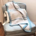 Textured crochet baby blanket on chair in cream and blue.